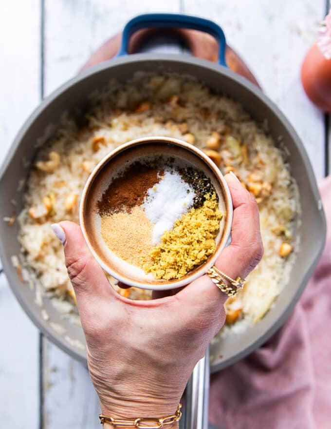 A hand holding a small plate of seasoning to add in to the rice 