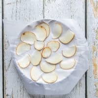 A ceramic plate with a layer of wax paper and then a single layer of potato slices spread over it