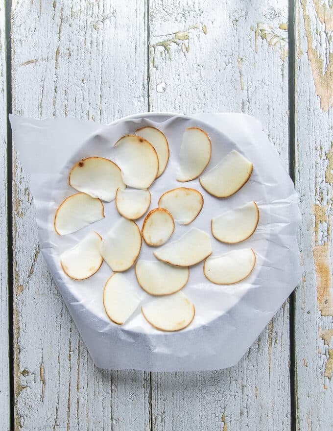 A ceramic plate with a layer of wax paper and then a single layer of potato slices spread over it 