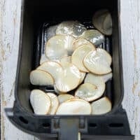 The thinly sliced and dried potatoes in the basket of the air fryer sprayed with some oil spray