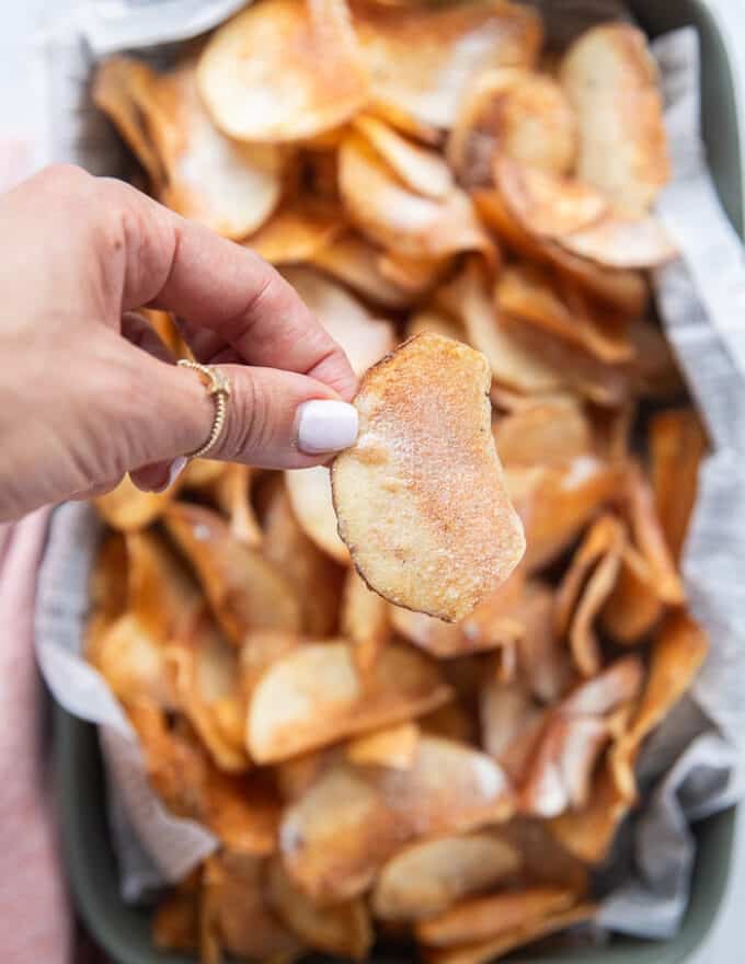 A hand holding a potato chip ready and seasoned close up showing the crispy texture and seasoning on top