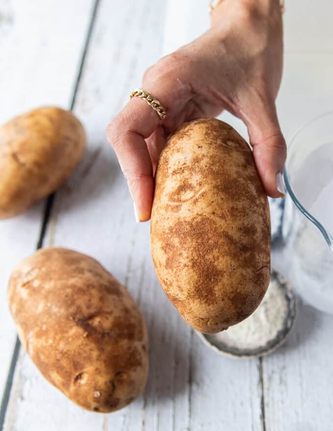 A hand holding a russet potato close up showing the best potatoes for potato chips 