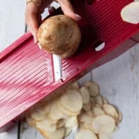 A hand slicing a russet potato using a mandolin slicer