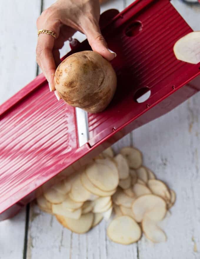 A hand slicing a russet potato using a mandolin slicer 