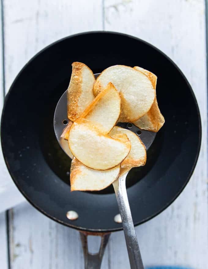 A slotted spoon slipping the chips in the hot oil 
