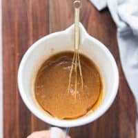 A hand holding a bowl of the miso marinade ingredients all whisked together using a small whisk