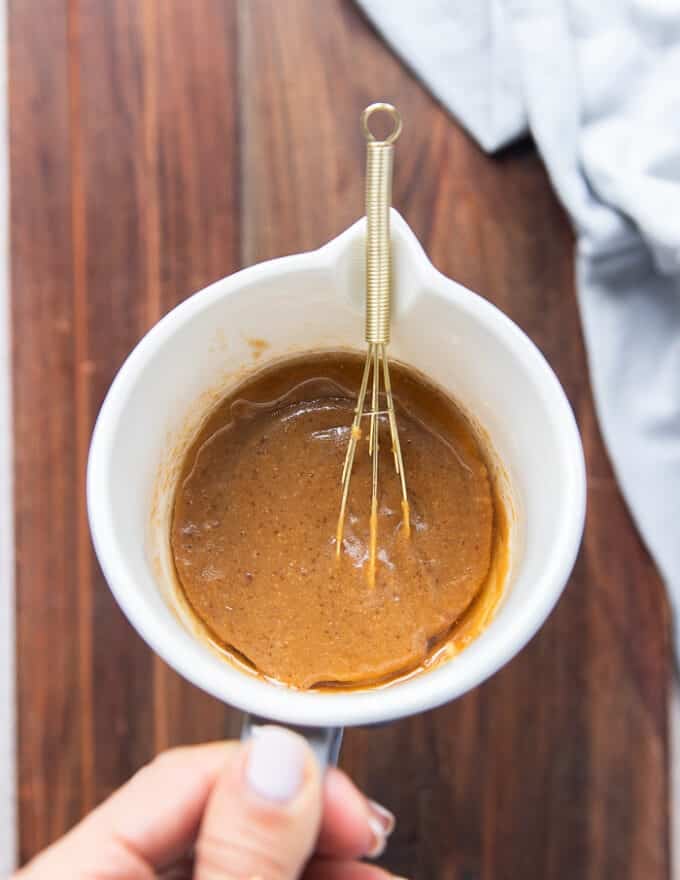 A hand holding a bowl of the miso marinade ingredients all whisked together using a small whisk