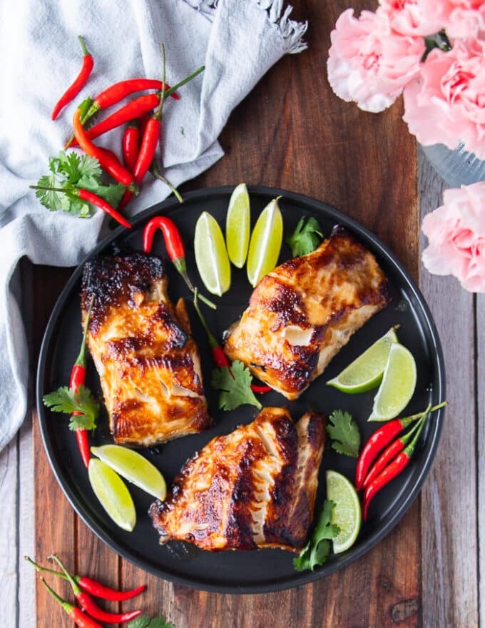 A plate of miso cod with three pieces of black cod with miso marinade, cooked until golden and surrounded with lime and red chillies 