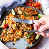 A hand holding a cut up piece of stuffed poblano pepers showing the filling inside the pepper