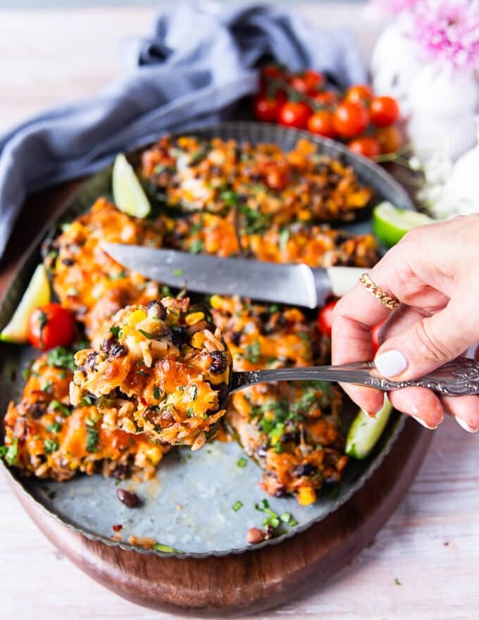 A hand holding a cut up piece of stuffed poblano pepers showing the filling inside the pepper