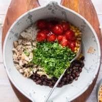 A large bowl with all the filling ingredients added in including rice, beans, tomatoes, corn, cilantro, cooked chicken