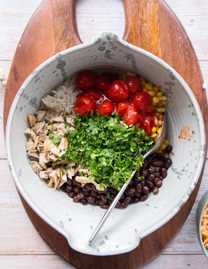 A large bowl with all the filling ingredients added in including rice, beans, tomatoes, corn, cilantro, cooked chicken