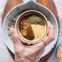A hand holding the seasoning blend of spices to add to the filling