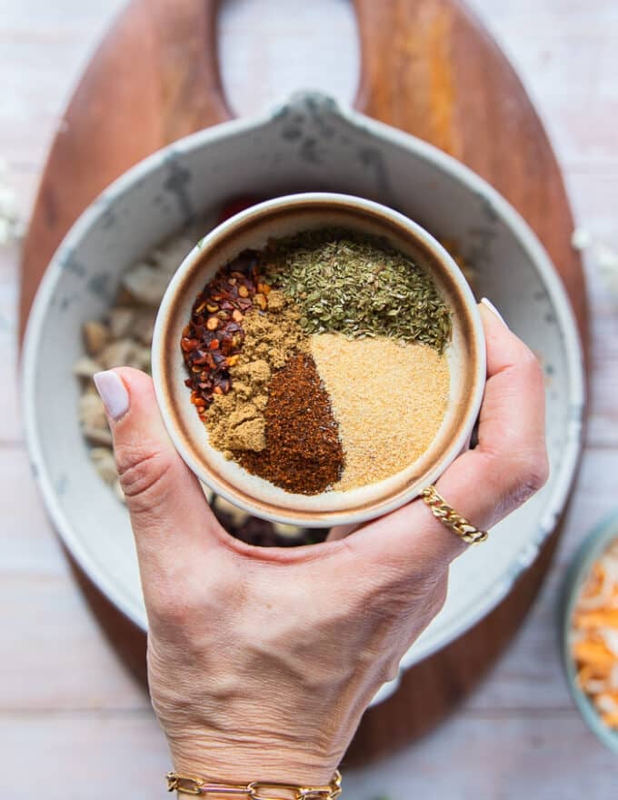A hand holding the seasoning blend of spices to add to the filling 
