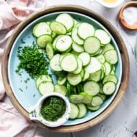 A bowl with thinly sliced cucumbers , diced onions and some of the dill