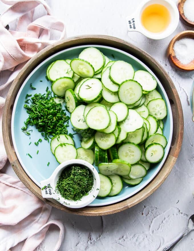 A bowl with thinly sliced cucumbers , diced onions and some of the dill