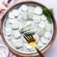 A hand holding creamy cucumber salad using a fork close up t the camera showing how creamy and perfect the cucumber salad is