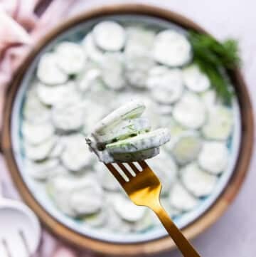 A hand holding creamy cucumber salad using a fork close up t the camera showing how creamy and perfect the cucumber salad is