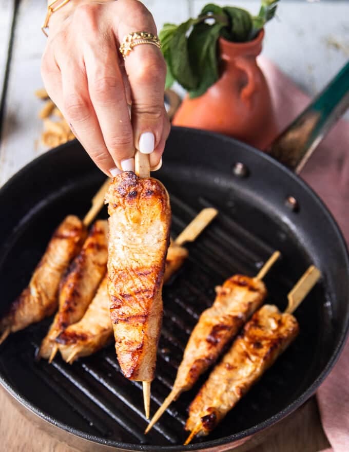 A hand holding a skewer of grilled halibut close up showing how perfectly cooked the fish is 