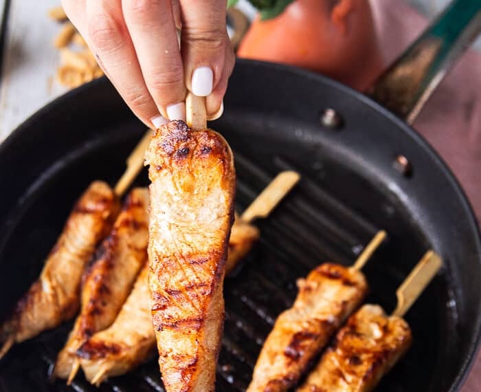 A hand holding a skewer of grilled halibut close up showing how perfectly cooked the fish is