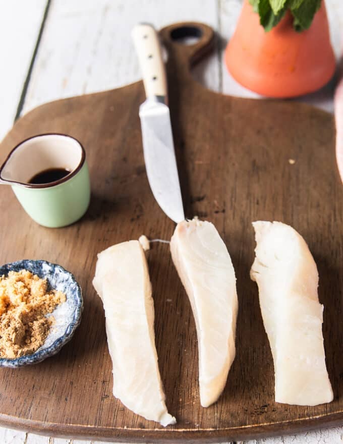 A piece of halibut fish cut into three long strips to grill