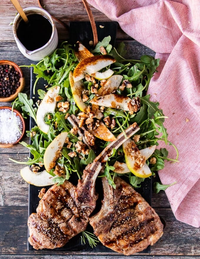 two perfectly grilled veal chops on a plate with some arugula salad on the side, drizzled with balsamic sauce