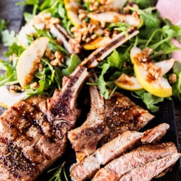 grilled veal chops on a board with one of them sliced to show how juicy it is served alongside a salad