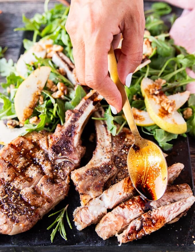 A hand using a spoon to drizzle some balsamic sauce over the grilled veal chops 