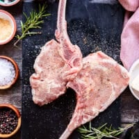two veal chops on a marbled board seasoned on both sides with salt, pepper and granulated garlic