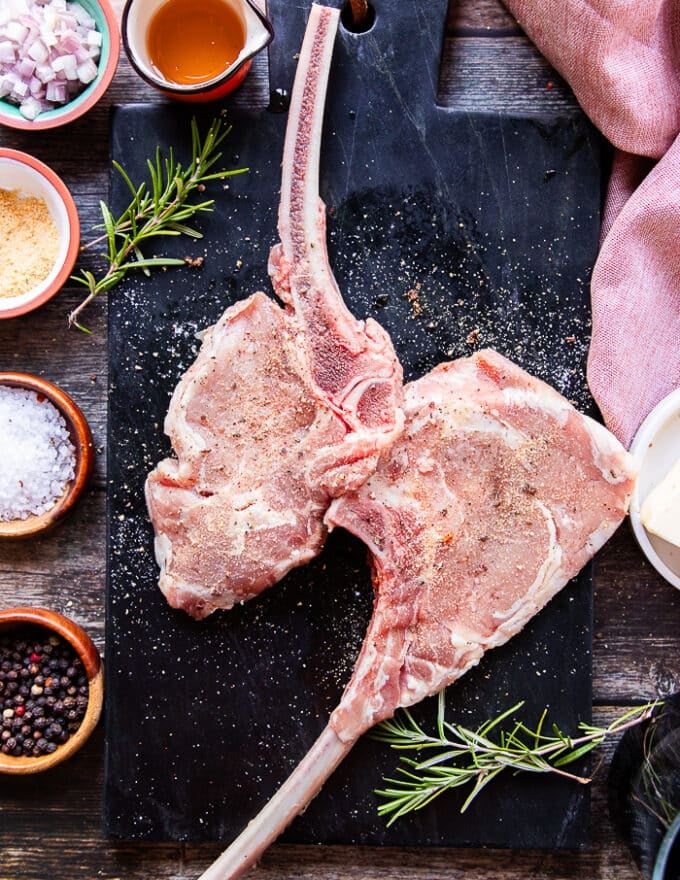 two veal chops on a marbled board seasoned on both sides with salt, pepper and granulated garlic 
