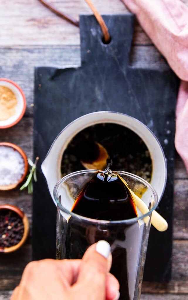 a hand pouring some balsamic vinegar in to a pot to make balsamic glaze 