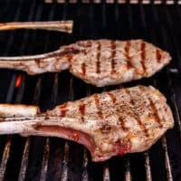 two veal chops on a grill flipped over showing the grill marks