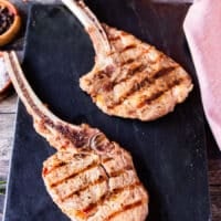 two perfectly grilled veal chops with grill marks resting on a marble after grilling