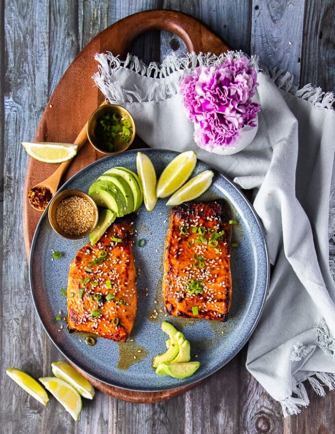 miso salmon on a plate garnished with sesame seeds, green onions and served with lime wedges and avocado slices