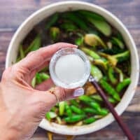 A hand holding a small cup of cornstarch mixed with water to make a slurry and ready to add in the Mongolian beef
