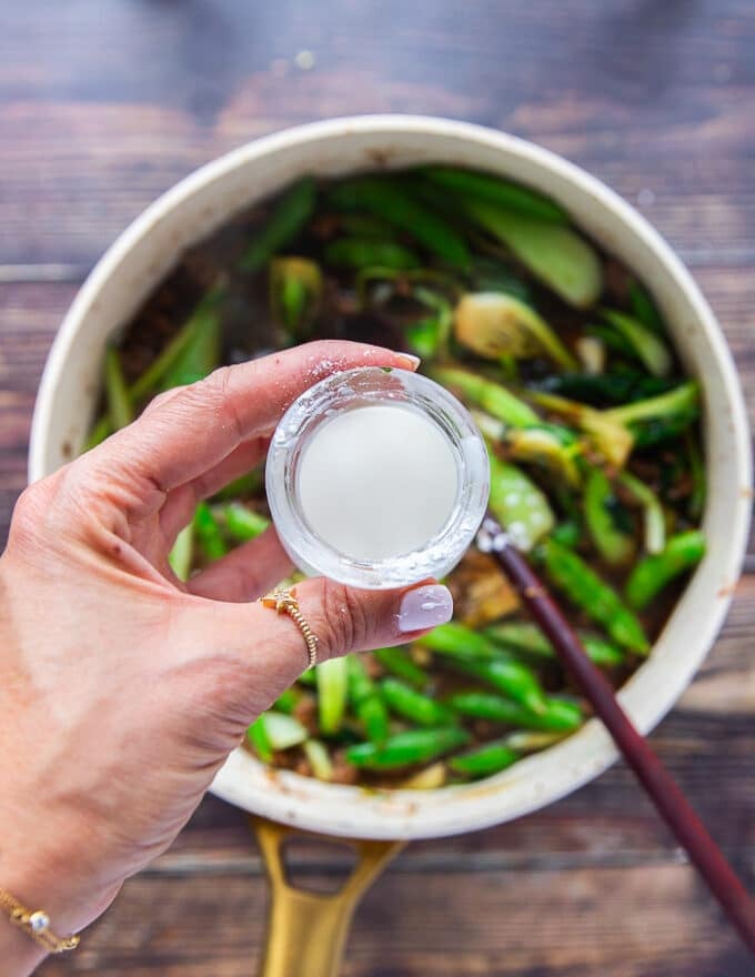 A hand holding a small cup of cornstarch mixed with water to make a slurry and ready to add in the Mongolian beef