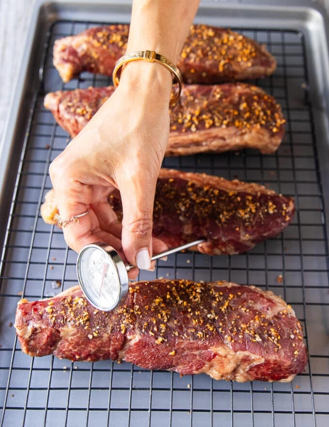 A hand holding a meat thermometer inserted into the steak to make sure the correct temperature has been reached '