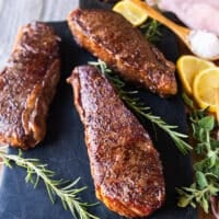 Three steaks on a board revere seared and perfectly browned on the outside and surrounded by lemon and rosemary