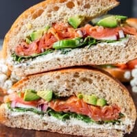 Super close up of a smoked salmon sandwich cut in half showing the layers os smoked salmon, avocados, cream cheese, arugula and cucumbers