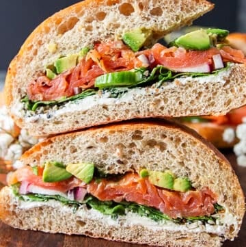 Super close up of a smoked salmon sandwich cut in half showing the layers os smoked salmon, avocados, cream cheese, arugula and cucumbers