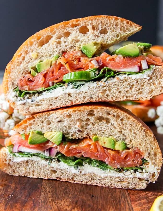 Super close up of a smoked salmon sandwich cut in half showing the layers os smoked salmon, avocados, cream cheese, arugula and cucumbers 