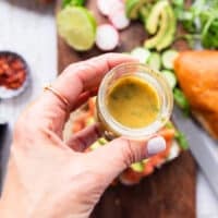 A hand holding the dill mustard sauce and ready to drizzle it over the smoked salmon to finish the sandwich