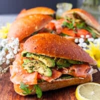 One smoked salmon sandwich on a board showing the layers of fillings and toppings close up surrounded by lemon slices