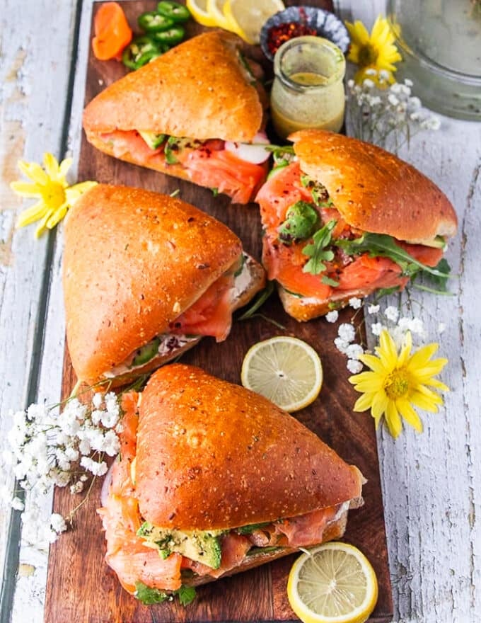 A board of 4 smoked salmon sandwiches ready and prepared, surrounded by lemon slices 