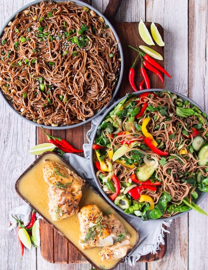 two plates of soba noodles, one warm and one cold, served with some buttery fish on the side