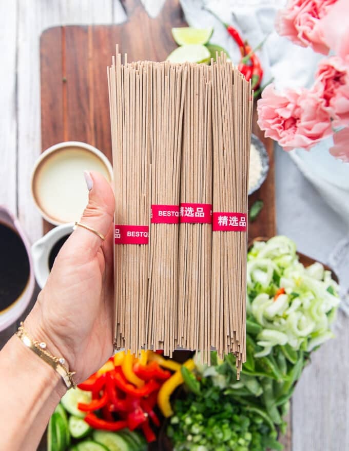 A hand holding a bunch of soba noodles showing how they look close up, raw and uncooked with the toasty color 