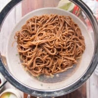 Soba noodles cooked in boiling water and drained in a sieve over a large bowl