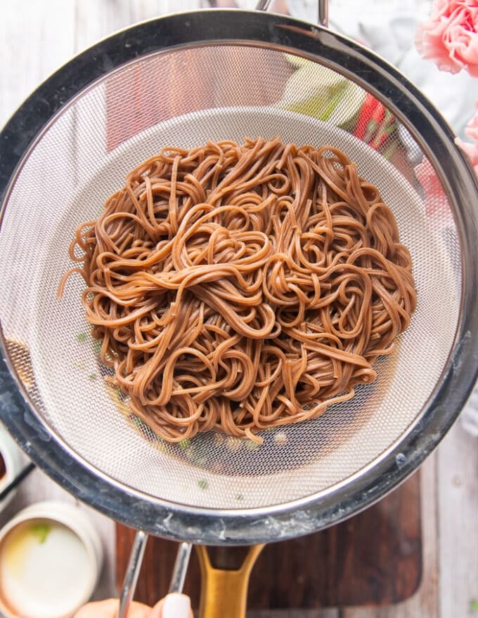 Soba noodles cooked in boiling water and drained in a sieve over a large bowl