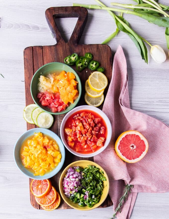 ingredients needed for citrus salsa including: segmented grapefruit, segmented oranges, blood orange, lemon, some diced onions in a bowl, diced jalapenos in a bowl, and minced cilantro in a bowl and salt 