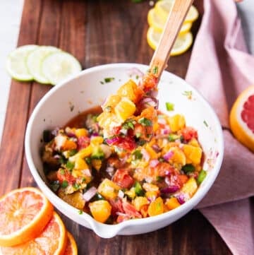 A spoon holing some citrus salsa close up showing the details and textures and how juicy the salsa